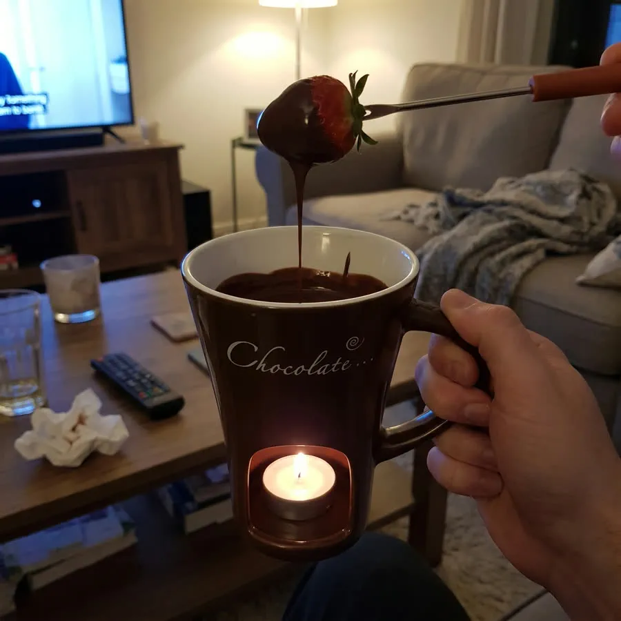 A couple on the sofa at night, one brown mug lit between them, a strawberry on the fork.