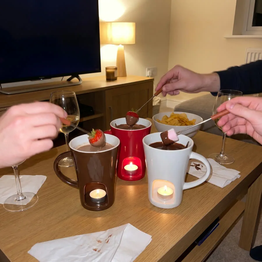 Four lit mugs in different colours on a coffee table, friends around it, a film on the screen behind.
